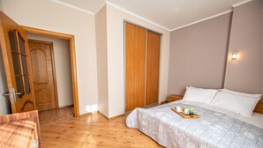 A bedroom with a wooden floor, a bed with a tray of items, a wardrobe, and a door. - WINWINSTAY Old Town City Apartment (Riga)
