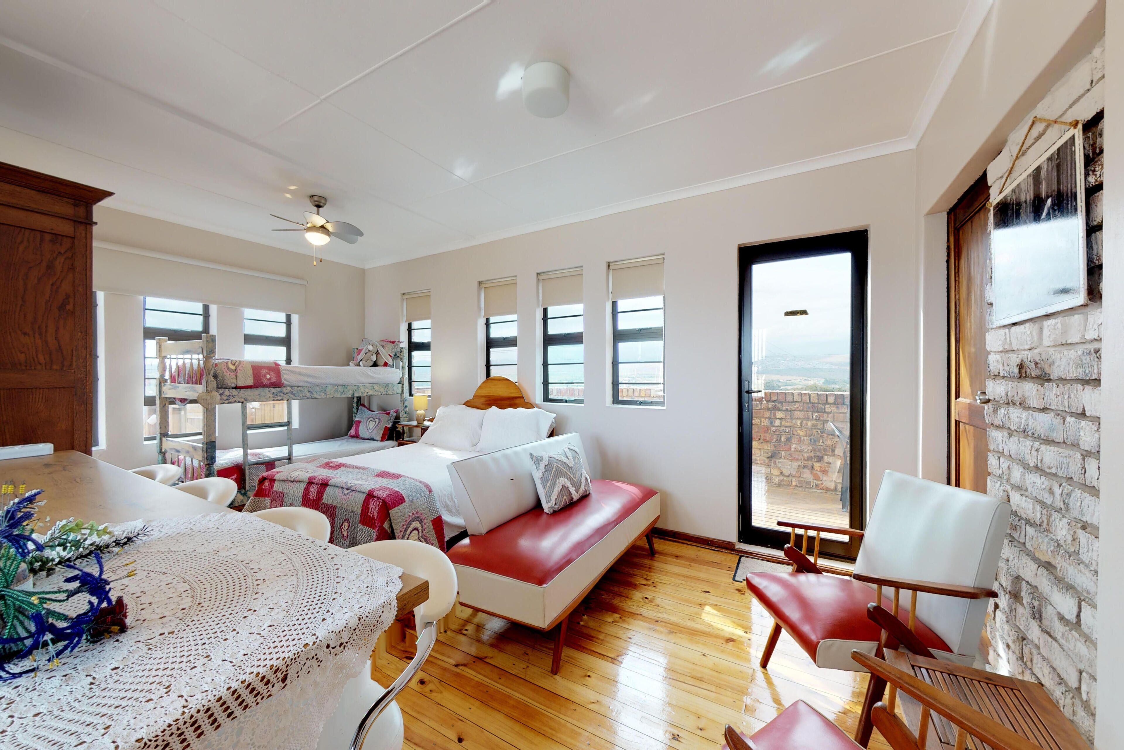 A spacious bedroom with a large bed, a red sofa, a dining table, and a view of the outdoors.