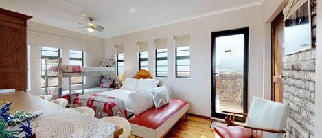 A spacious bedroom with a large bed, a red sofa, a dining table, and a view of the outdoors.
