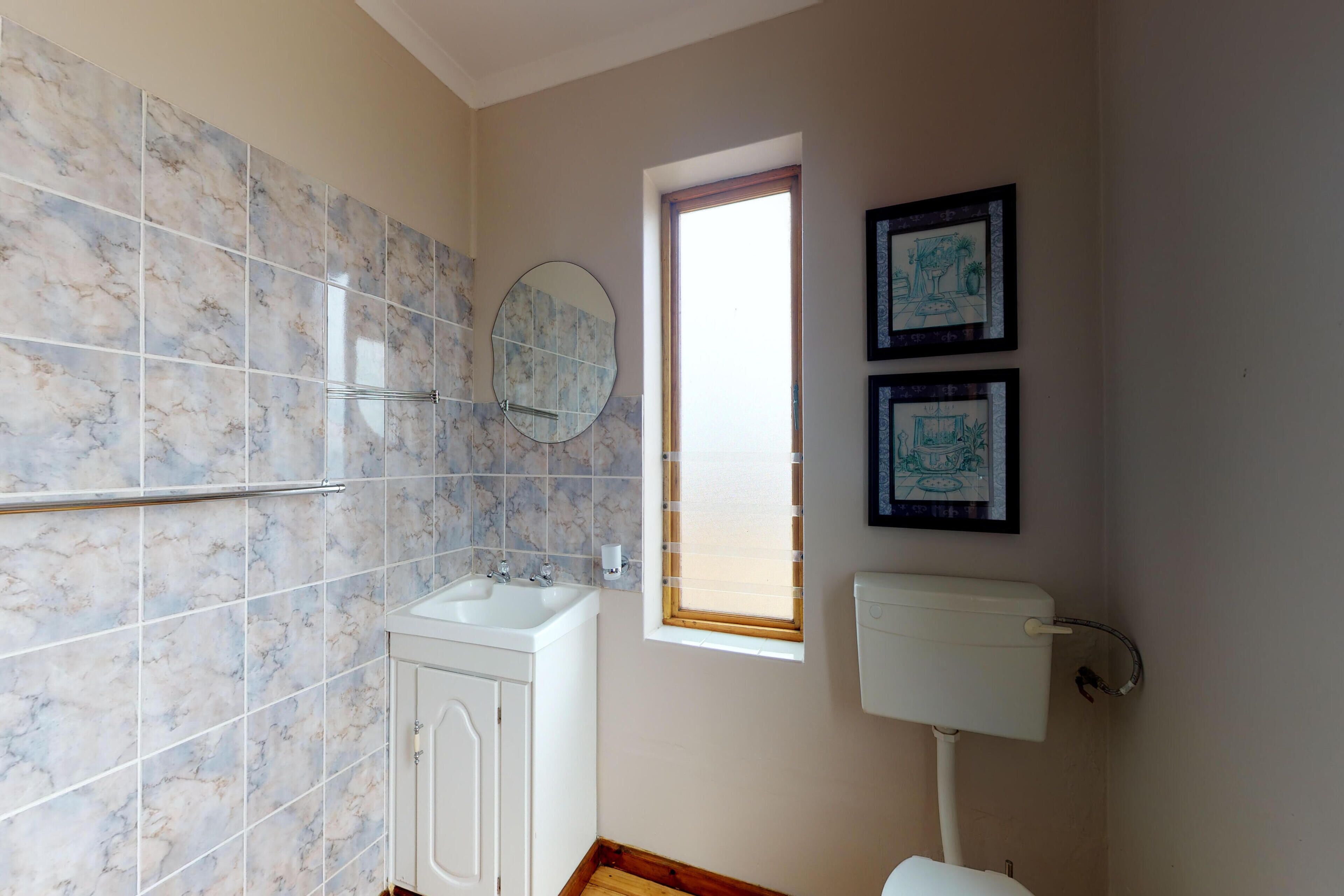A bathroom with marble tiles, a sink, a mirror, a toilet, and two framed pictures on the wall.