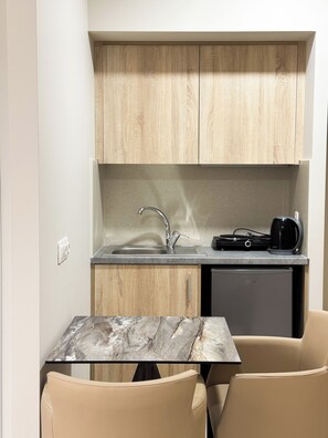 A compact kitchenette with a sink, a coffee maker, and a small refrigerator. There is a glass table with a marble-like top and two beige chairs. - Acropolis Apartments (Hersonissos)