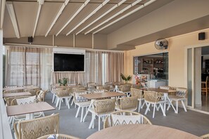 Un restaurant doté de nombreuses tables et chaises, d’un écran de télévision et d’un bar avec des étagères remplies de bouteilles.
