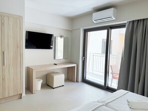 A hotel room with a bed, a desk, a television, a mirror, an air conditioning unit, a balcony with a railing, and a window with curtains. - Acropolis Apartments (Hersonissos)