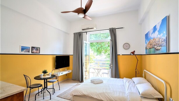 A hotel room with a bed, a desk with a chair, a TV, and a painting on the wall. - Salame TLV Apartments (Tel Aviv)
