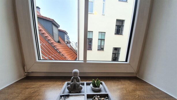 A small stone tray with a Buddha statue, a potted plant, and a collection of stones on a wooden floor, viewed through a window overlooking buildings. - WINWINSTAY Old Town Riverside Apartment (Riga)