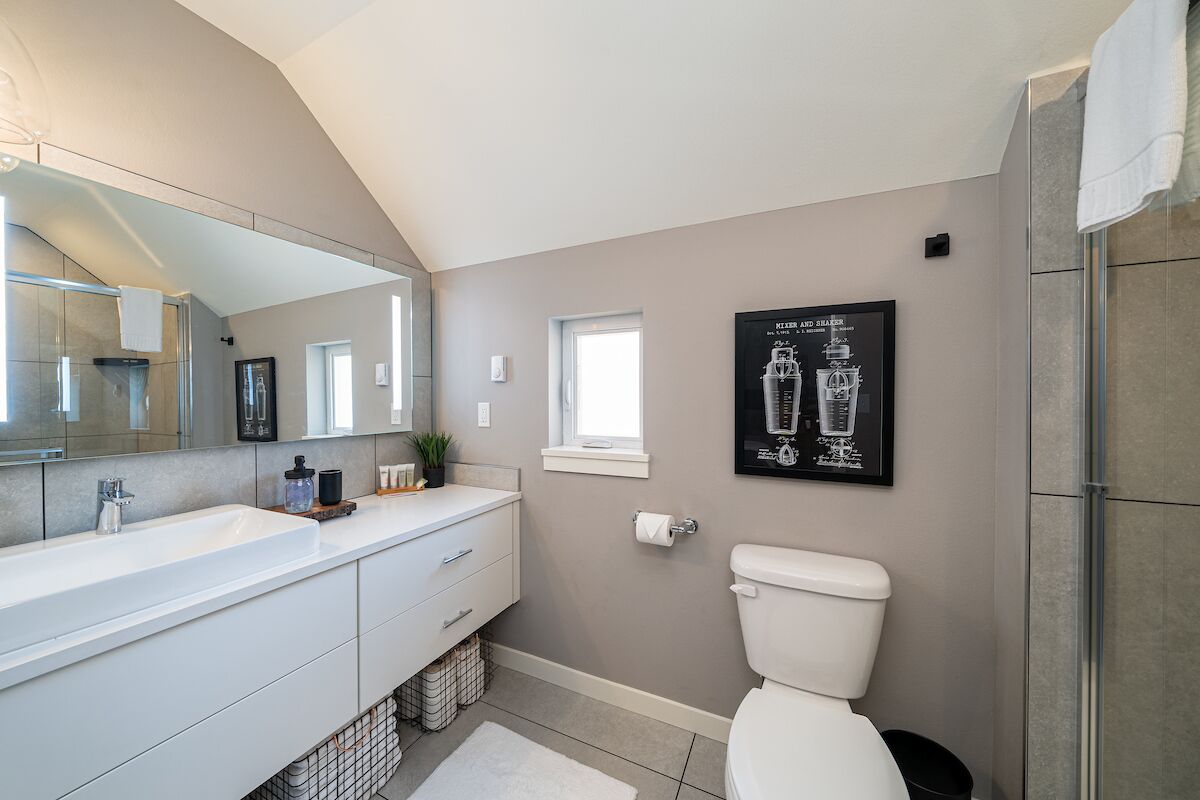 Une salle de bain moderne avec un grand miroir, un lavabo blanc, des toilettes et un espace douche.