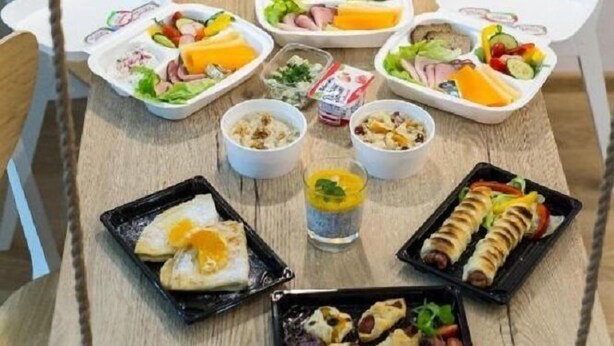 Une table en bois sur laquelle se trouvent divers aliments et récipients, notamment des sandwichs, des salades et un hot-dog.