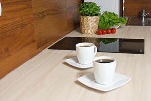 A kitchen with a wooden countertop, two white coffee cups on saucers, a woven basket with green plants, and a sink. - Apart-Center Motyl (Zakopane)