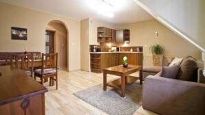 Un salon comprenant une table à manger en bois, un canapé et un coin cuisine avec des meubles de rangement en bois et un plan de travail.