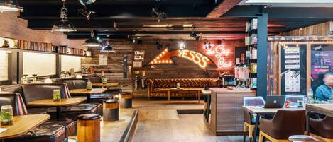 Un restaurant chaleureux avec des tables et des banquettes en bois, un panneau lumineux au néon et un tableau affichant le menu.