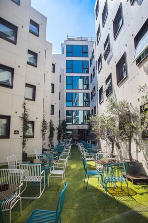 A courtyard with rows of blue chairs and tables, surrounded by white buildings with multiple windows. - 1n Student Hotel Camden - Students Only (London)