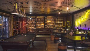 Un espace intérieur accueillant, doté d’une table de billard, de bibliothèques et d’un panneau néon sur lequel on peut lire « STAY CLUB ».