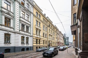Une rue bordée de bâtiments historiques, où sont garées des voitures, et dont la chaussée est pavée.