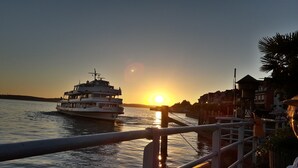 Un coucher de soleil sur une étendue d’eau, avec un bateau portant le nom « MUNCHEN » et une jetée bordée de bâtiments en arrière-plan.