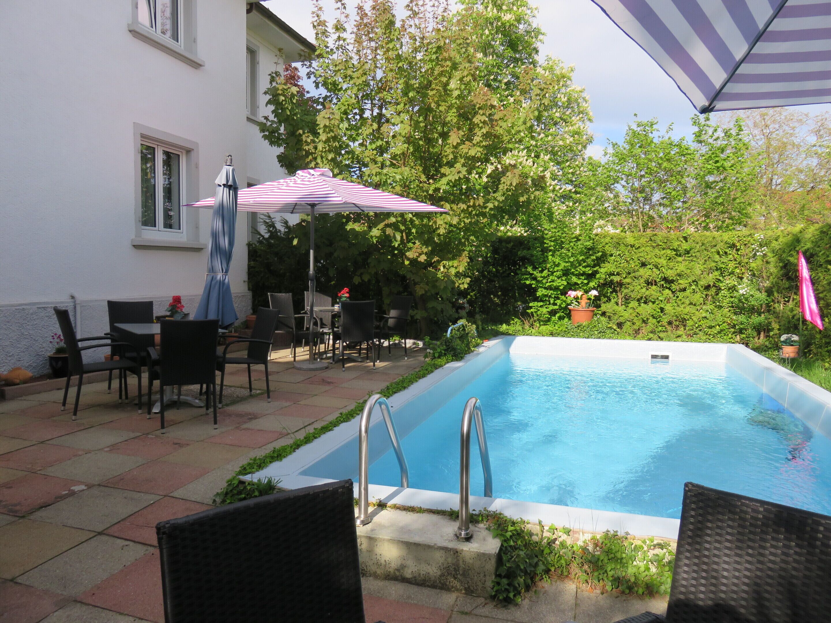 A swimming pool with a metal ladder, surrounded by outdoor furniture and a covered patio area.