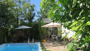 Une piscine avec un escalier, entourée d’une terrasse aménagée avec des meubles d’extérieur et des parasols.
