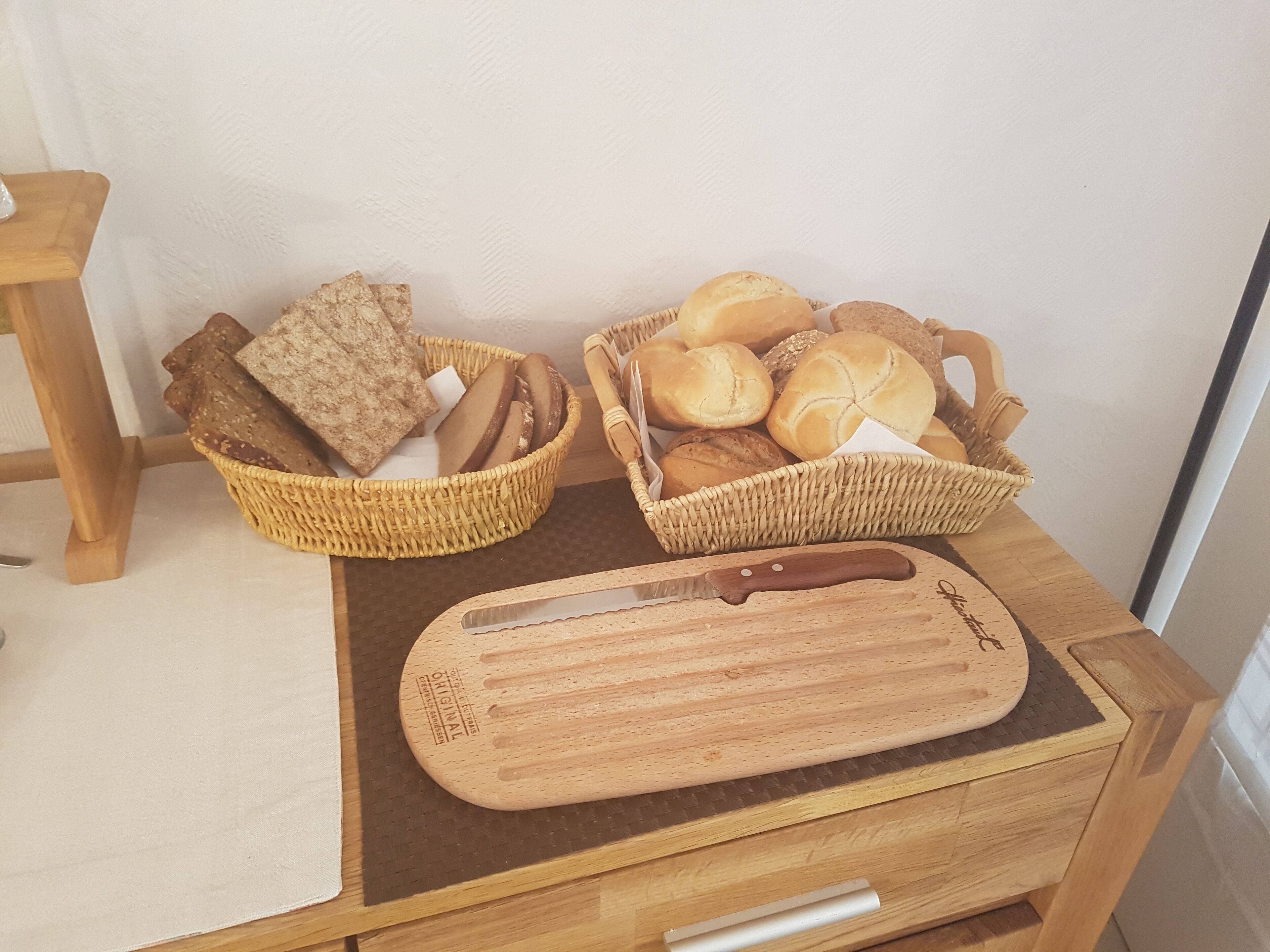 Dos cestas de mimbre llenas de panes variados y una tabla de madera con un cuchillo sobre una mesa de madera.