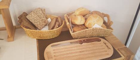 Dos cestas de mimbre llenas de panes variados y una tabla de madera con un cuchillo sobre una mesa de madera.