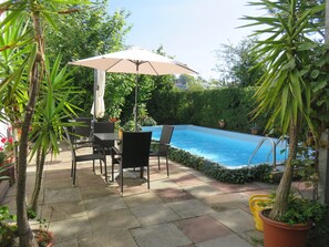 A poolside patio with a table and chairs, surrounded by potted plants and a swimming pool. - Pension Säntisblick (Meersburg)