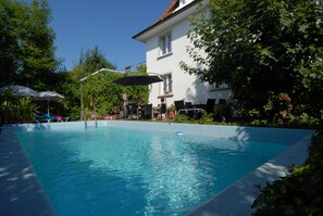 A rectangular swimming pool with a white house in the background. - Pension Säntisblick (Meersburg)