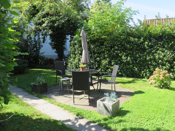 An outdoor patio with a table and chairs, surrounded by greenery and a hedge. - Pension Säntisblick (Meersburg)