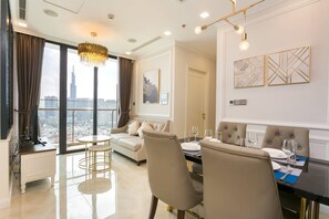 A modern hotel room with a dining area, a sofa, and a large window offering a city view.
