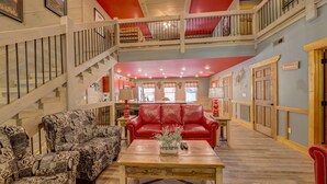 A spacious living area with a red sofa, patterned armchairs, and a wooden coffee table. A staircase with a railing leads to an upper level. - Blue Lagoon Cinema (Gatlinburg)