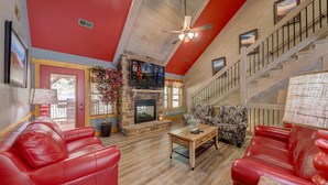 A spacious living room with a stone fireplace, red leather sofas, and a wooden coffee table. - Blue Lagoon Cinema (Gatlinburg)
