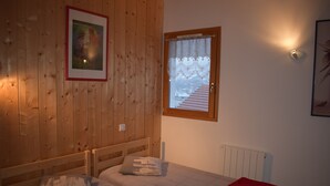 A room with wooden walls, a bed with a red blanket, a window with a view of a snowy landscape, and a framed picture on the wall.