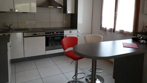 A modern kitchen with white cabinets, a stainless steel range hood, a built-in oven, and a red bar stool.