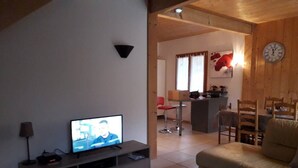 A living room with a television, a sofa, a coffee table with a bowl of ornaments, and a kitchen area in the background.