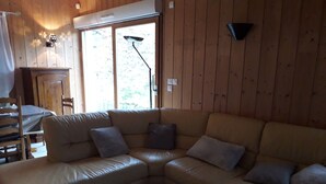 A cozy living room with a beige leather sectional sofa, a dining table with chairs, and a large window providing natural light.
