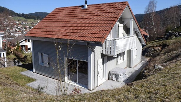 A two-story house with a red-tiled roof, a balcony, and a garage.