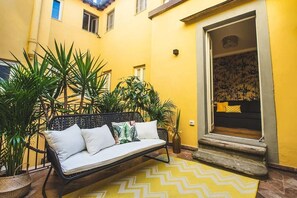 Un edificio amarillo con un banco de metal negro y plantas en macetas.