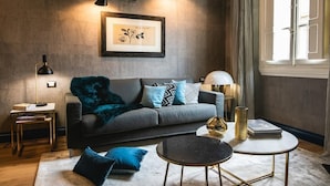 Un salon moderne avec un canapé gris, des coussins bleus, une table basse ronde et une œuvre d’art encadrée accrochée au mur.