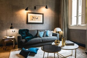Una sala de estar moderna con un sofá gris, cojines azules, una mesa redonda de centro y una obra enmarcada en la pared.
