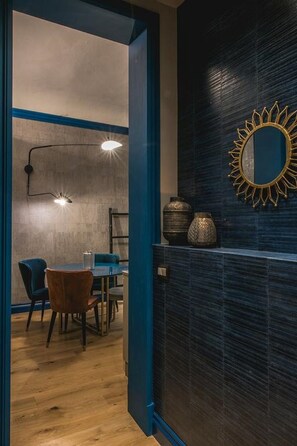 Un interior moderno con una zona de comedor que presenta una mesa y sillas de madera, una pared azul decorativa y un espejo con diseño de sol.