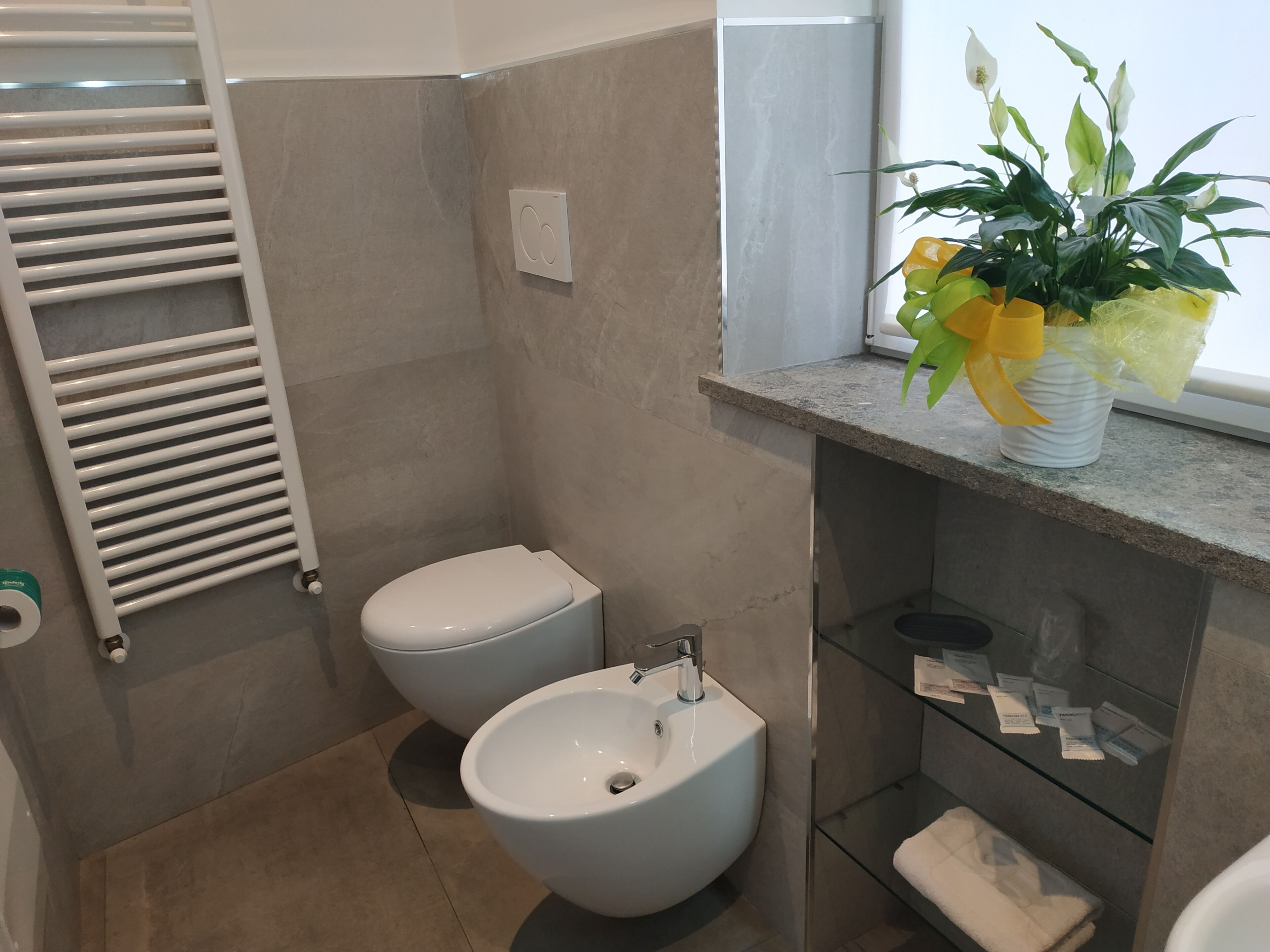 Un baño moderno con bidé, inodoro y estante de vidrio con artículos de aseo.