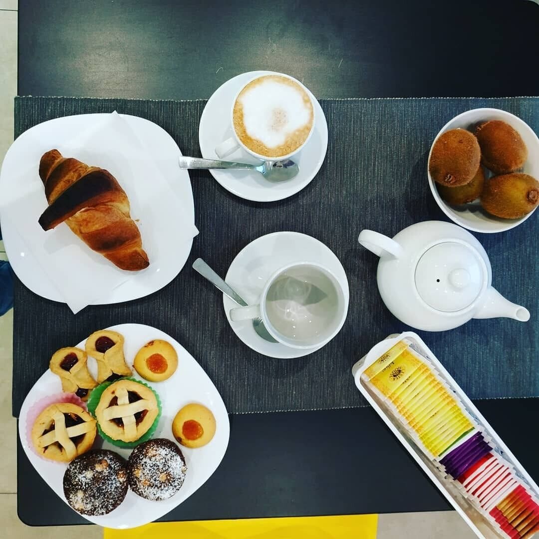 Ein Tisch mit einem Croissant, einer Kaffeetasse, einem Teekessel, einem Teller mit Gebäck und einer Schachtel bunter Stifte.