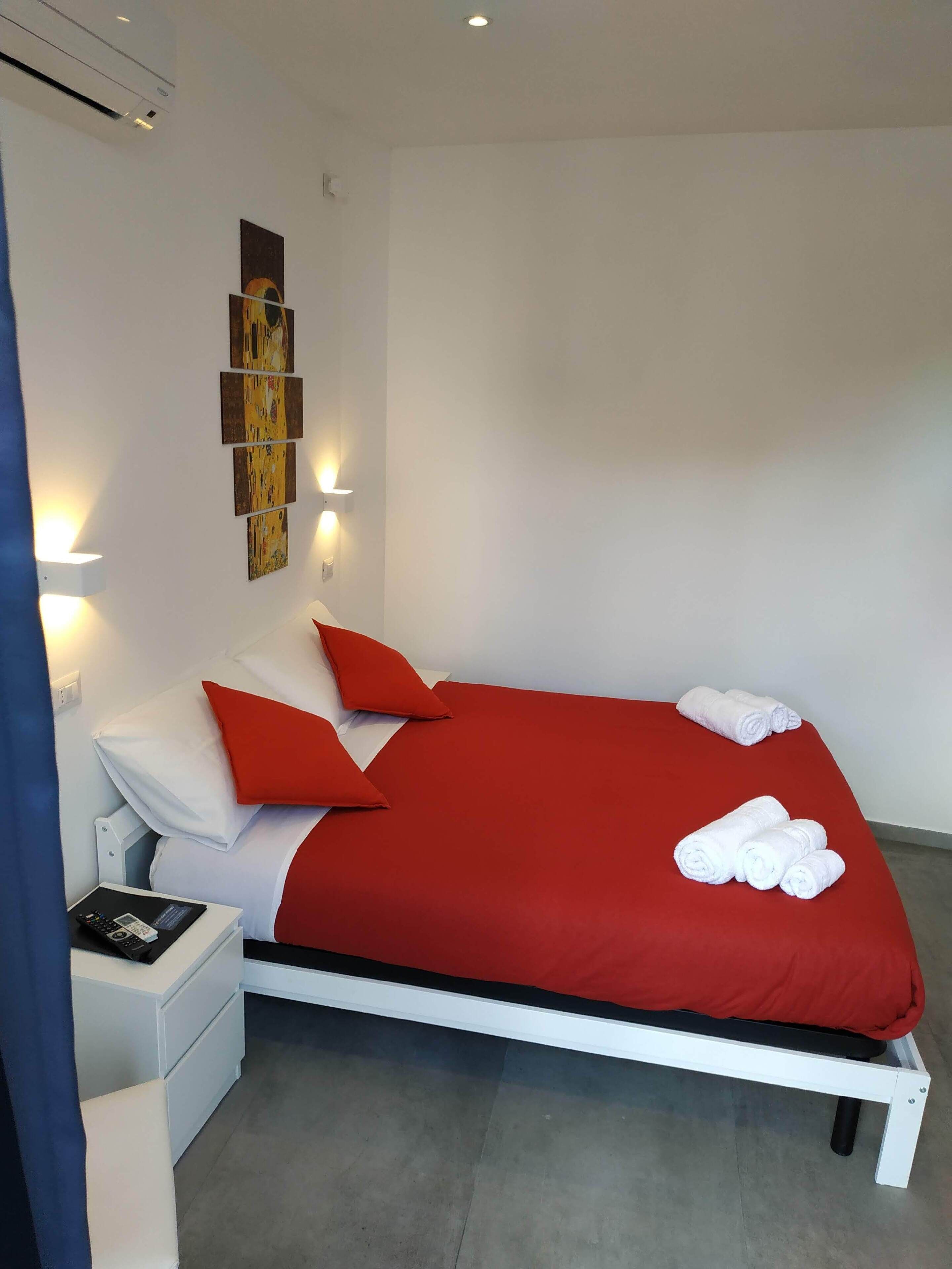 Ein modernes Hotelzimmer mit einem weißen Bett, roter Bettwäsche und einem Nachttisch mit Fernbedienung.