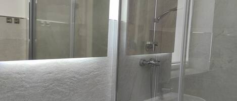 Un bagno moderno con cabina doccia in vetro, lavabo bianco e specchio.