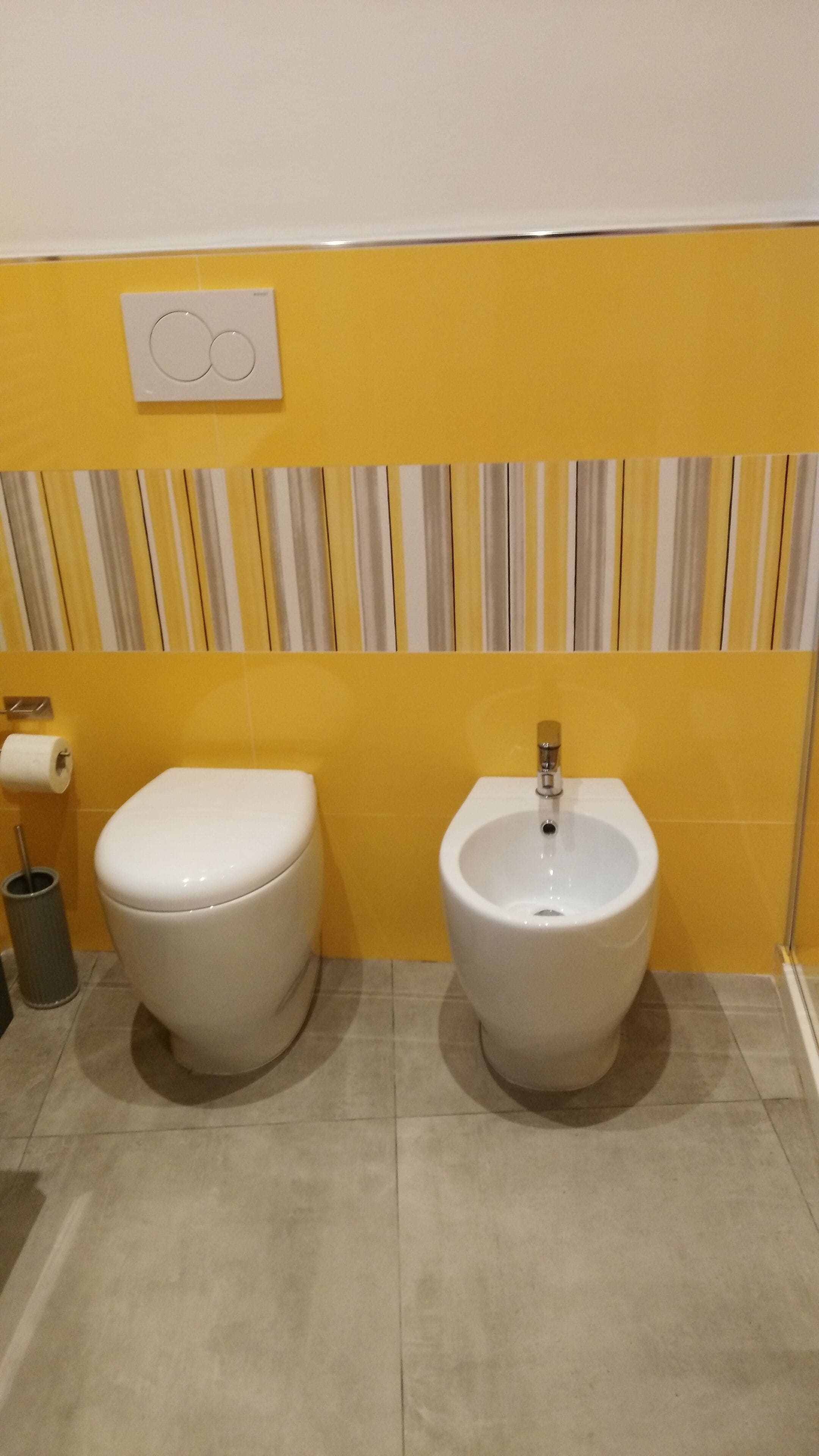 Une salle de bain avec des toilettes et un bidet, des murs jaunes, un papier peint à rayures et une poubelle.