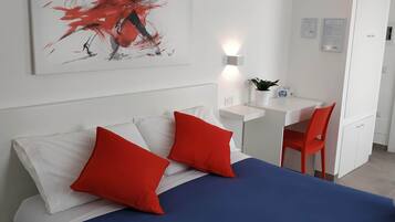 Una camera d'albergo moderna con un letto grande, cuscini rossi, una scrivania e una sedia.
