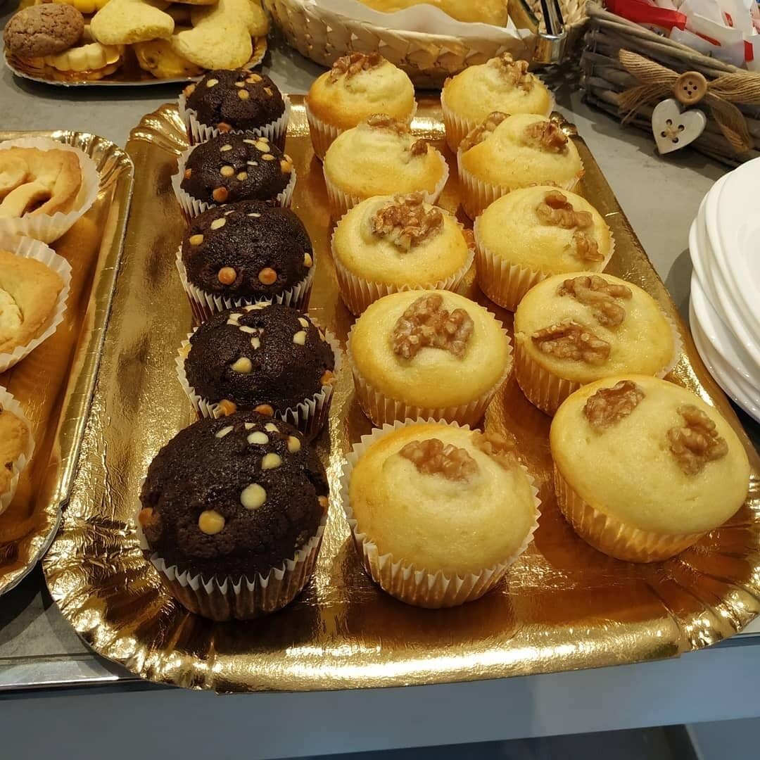 A tray of assorted muffins and cookies, some topped with walnuts, on a reflective surface.