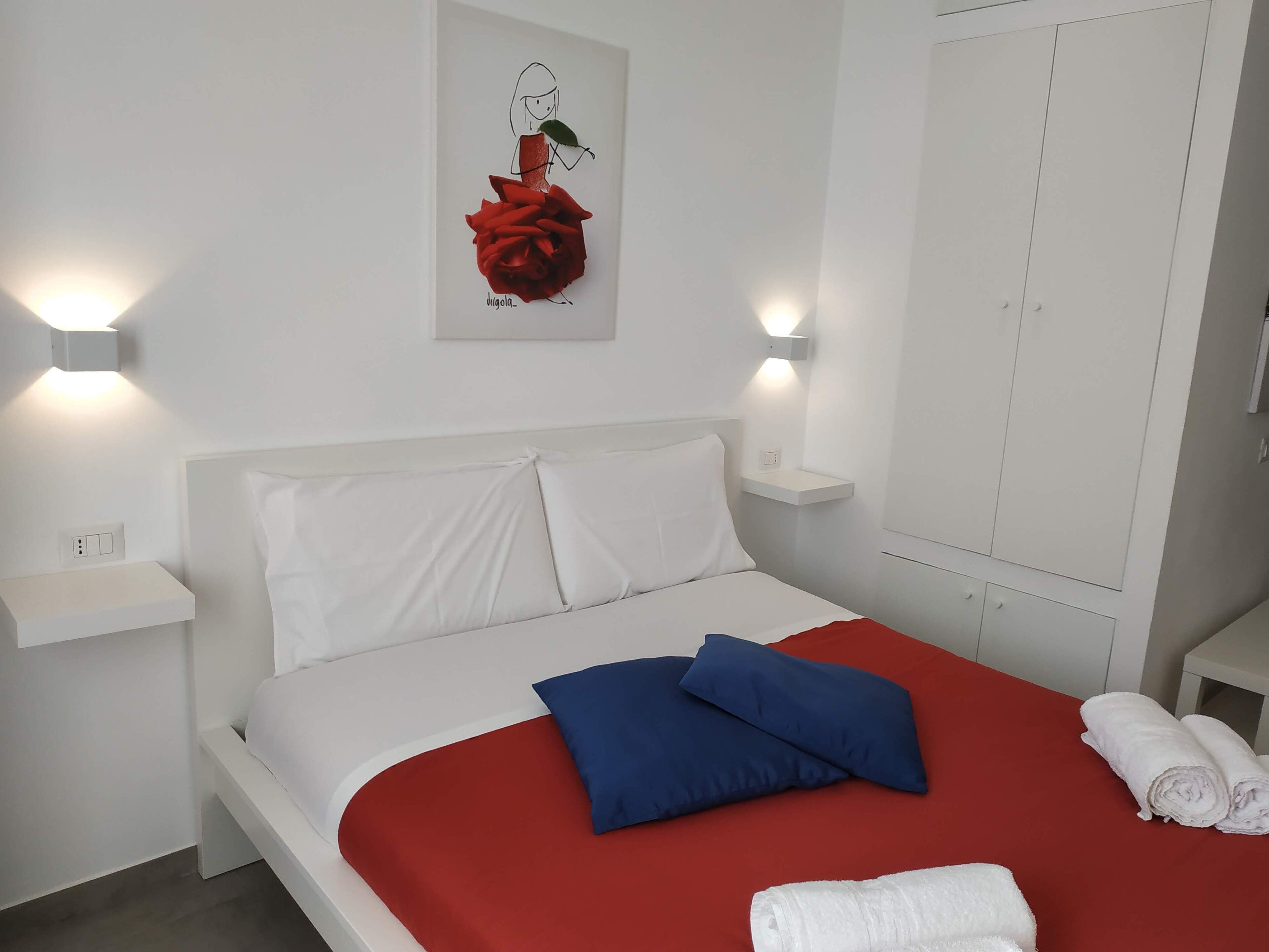 A neatly made bed with white and red bedding, a blue pillow, and white towels.