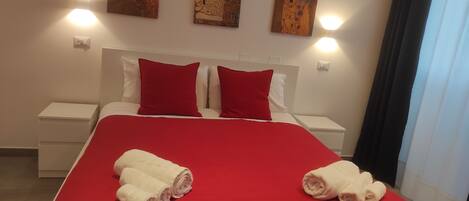 A hotel room with a large bed, red bedding, two red pillows, white nightstands, and three wall-mounted paintings.