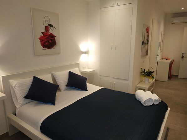 A neatly made bed with white and navy bedding, a bedside table with a lamp, and a wardrobe with a mirror. - Palazzo Verdi B&B (Viterbo)