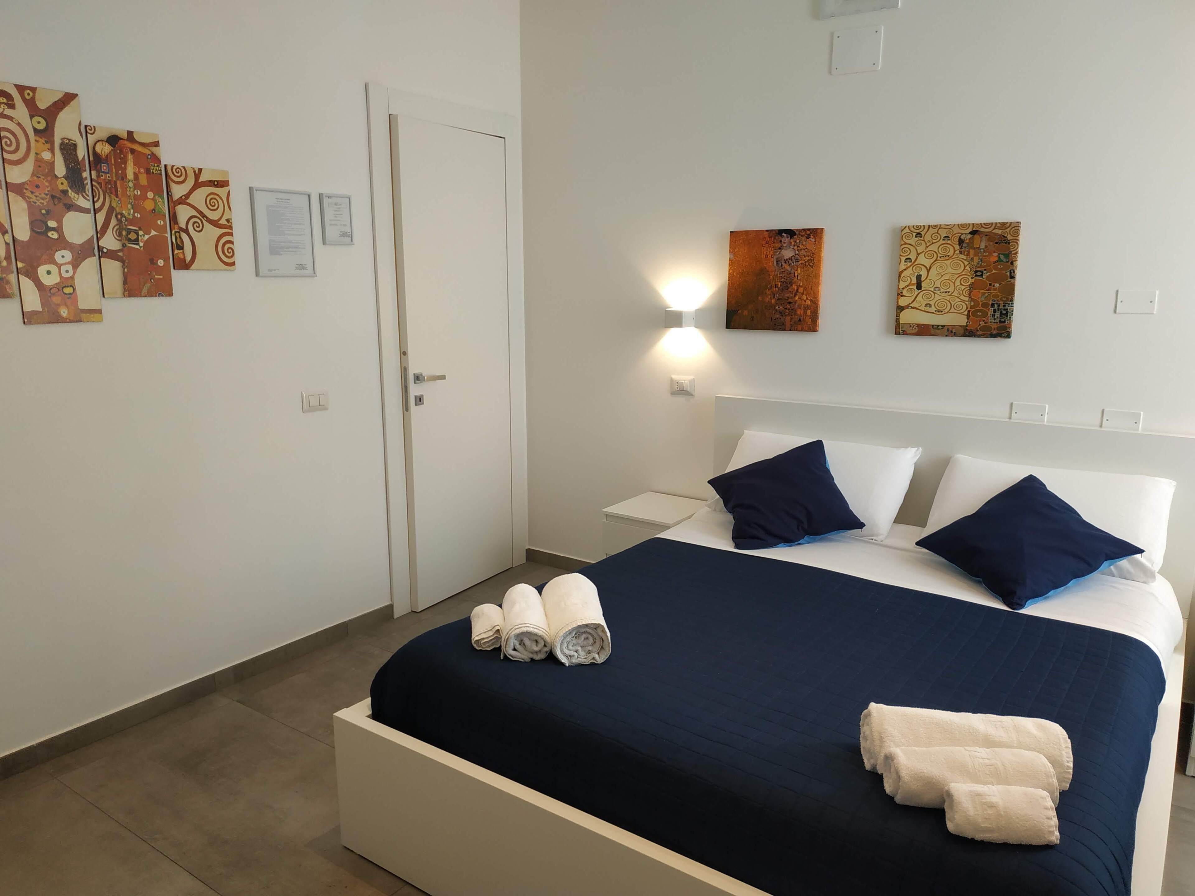 A hotel room with a large bed, white walls, and artwork on the walls.