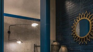 Un intérieur moderne avec un coin repas comprenant une table et des chaises en bois, un mur d’accent bleu et un miroir décoratif en forme de soleil.