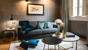 Un salon moderne avec un canapé gris, des coussins bleus, une table basse ronde et une œuvre d’art encadrée accrochée au mur.